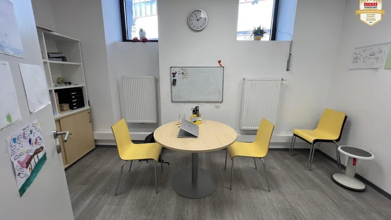 Heller Büroraum mit Holztisch, gelben Stühlen und zwei Fenstern, ideal für Besprechungen.