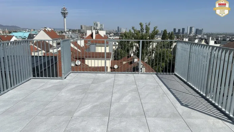 Große Dachterrasse mit Fliesenboden und weitem Blick über die Stadt und den Donauturm.