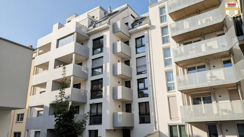 Modernes Mehrfamilienhaus mit vielen Balkonen und großen Fenstern unter blauem Himmel.