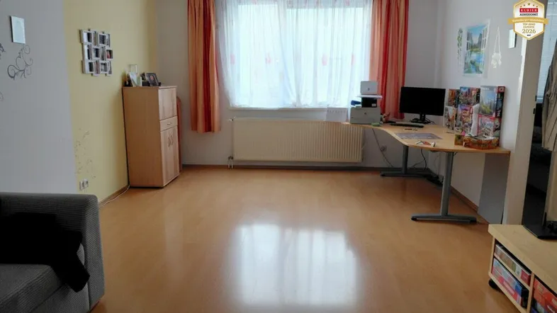 Helles Wohnzimmer mit Laminatboden, einem Schreibtisch und einem bequemen Sofa.