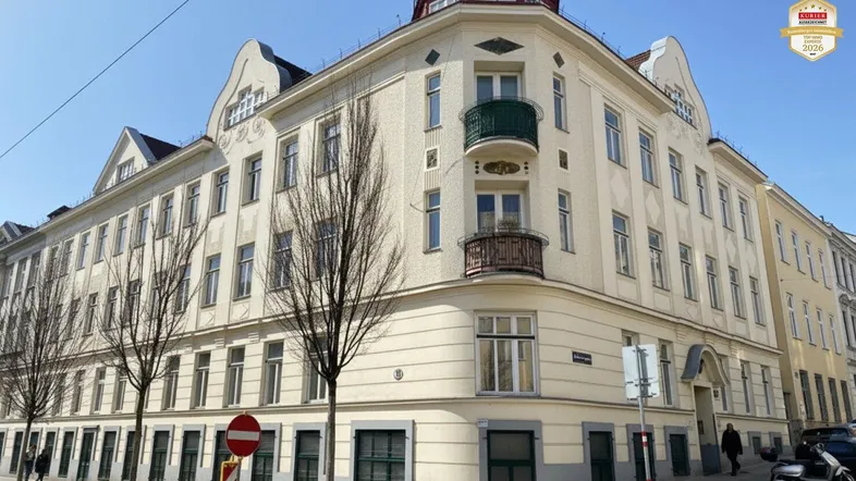 Historisches Eckgebäude mit mehreren Stockwerken und klassischen Balkonen unter blauem Himmel.