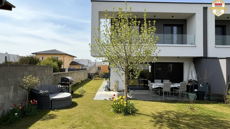 Moderner Gartenbereich mit Rasenfläche, Terrasse und Sitzgelegenheiten hinter dem Haus.