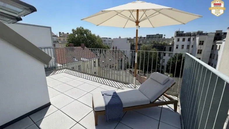 Sonnige Dachterrasse mit bequemer Liege, Sonnenschirm und weitem Blick über die Stadt.