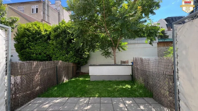 Gepflasterte Terrasse mit kleinem Rasenbereich und Baum, umgeben von einem Zaun.