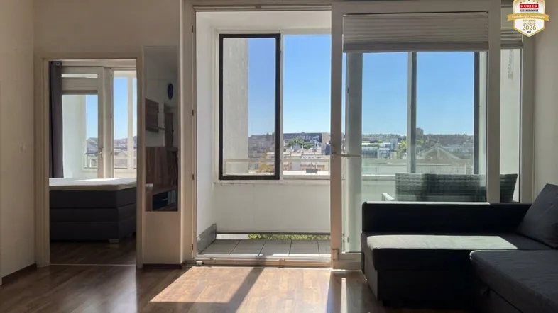 Helles Wohnzimmer mit Holzboden, Sofa und Zugang zum Balkon mit Stadtblick.
