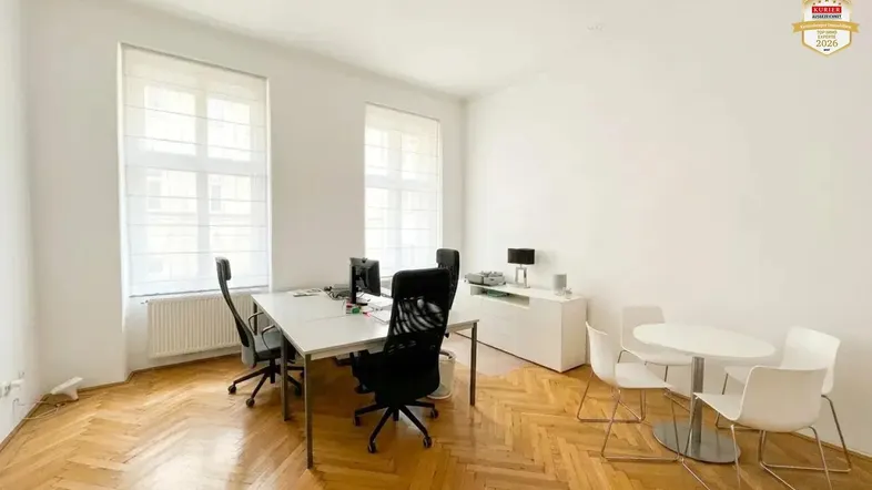 Geräumiges Büro mit Fischgrätparkett, weißen Wänden und viel Tageslicht durch große Fenster.