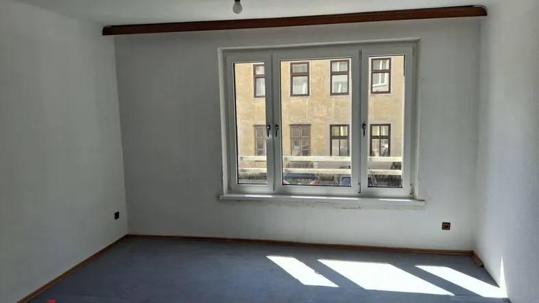 Helles Zimmer mit großem Fenster und Blick auf die gegenüberliegende Fassade, bereit zur individuellen Gestaltung.
