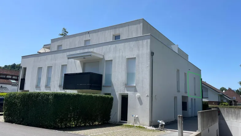Modernes Mehrfamilienhaus mit weißer Fassade, Balkon und gepflegter Hecke im Außenbereich.