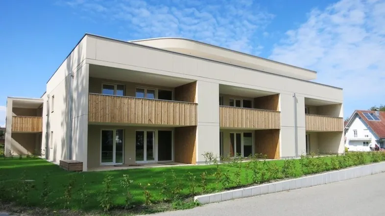 Modernes Mehrfamilienhaus mit heller Fassade, Holzverkleidung und Balkonen unter blauem Himmel.