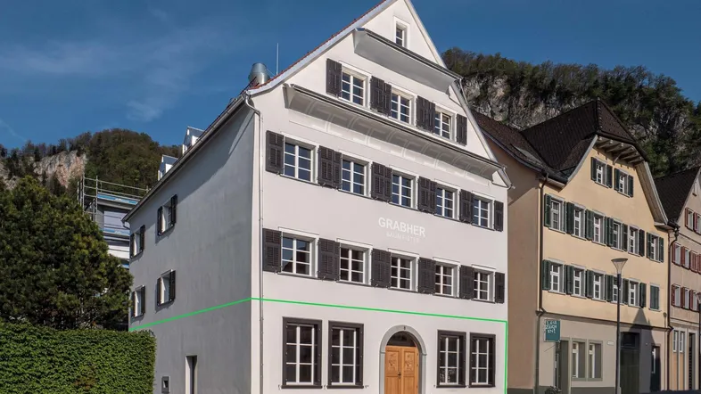 Historisches Gebäude mit weißer Fassade, vielen Fenstern und dunklen Fensterläden in einer Gasse.
