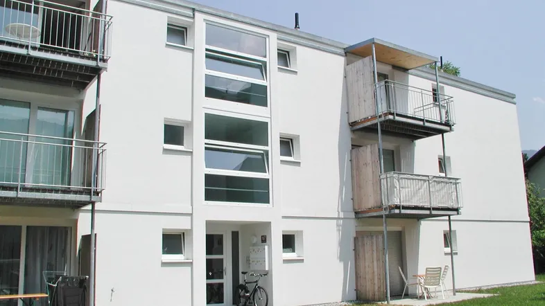Modernes Mehrfamilienhaus mit weißer Fassade, großen Fenstern und Balkonen in grüner Umgebung.