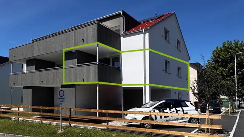 Modernes Mehrfamilienhaus mit Balkonen und Carport-Bereich unter blauem Himmel.
