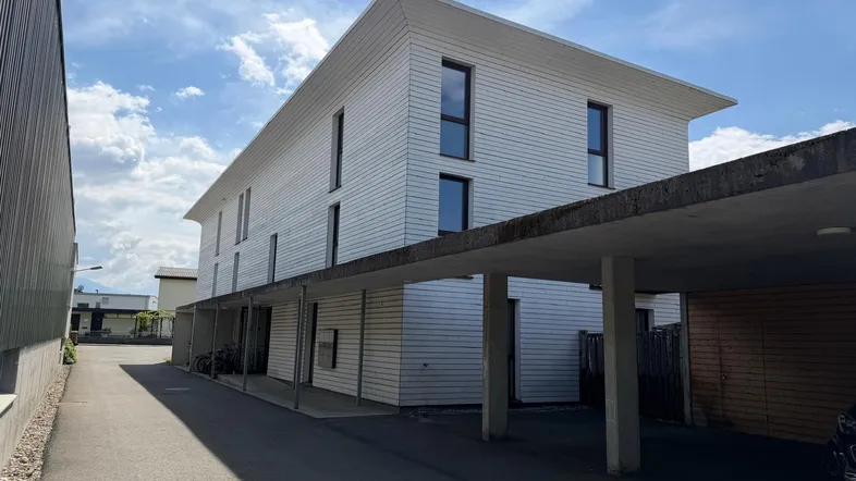 Modernes Mehrfamilienhaus mit weißer Fassade und überdachten Parkplätzen unter einem Carport.
