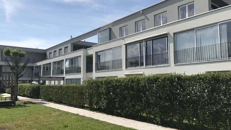 Moderne Wohnanlage mit großen Fenstern, Balkonen und gepflegter Hecke vor einer Grünfläche.