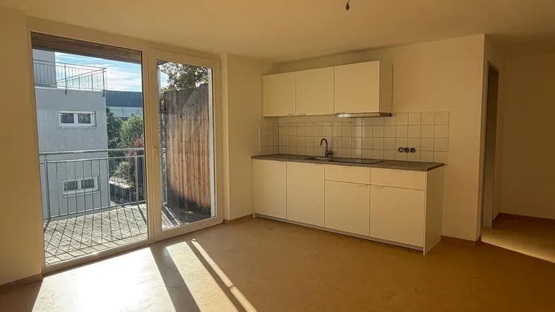 Helles Zimmer mit integrierter Küchenzeile und Zugang zu einem sonnigen Balkon, ideal für ein Studio-Apartment.