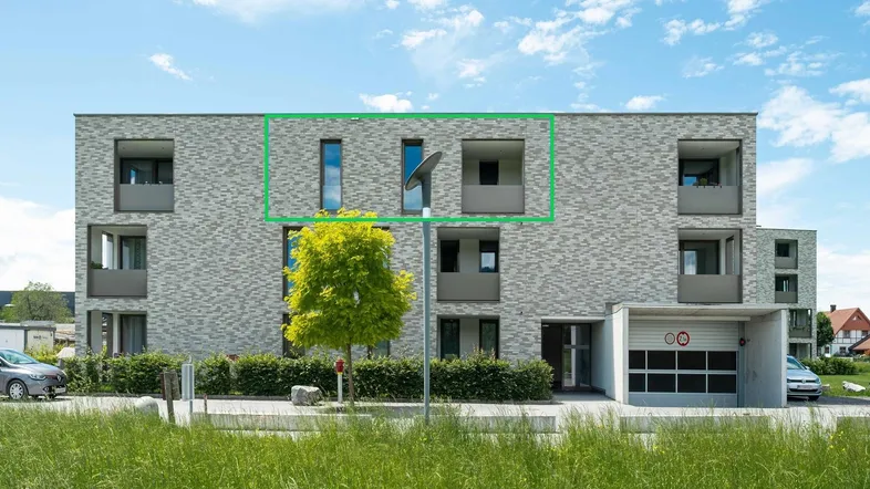 Modernes Mehrfamilienhaus mit heller Ziegelfassade, großen Fenstern und Tiefgaragenzufahrt.