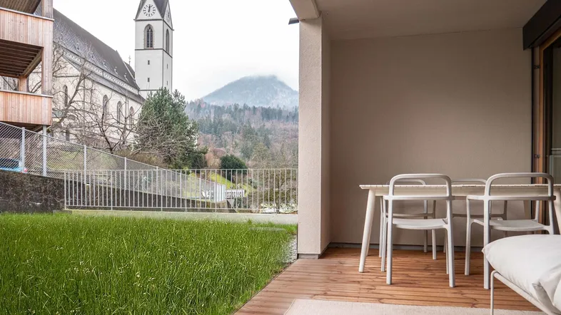 Geräumige Terrasse mit Holzboden, Sitzgelegenheiten und Blick auf die Kirche und Berge.