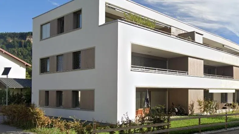 Modernes Mehrfamilienhaus mit weißer Fassade, Balkonen und Terrassen in grüner Umgebung.