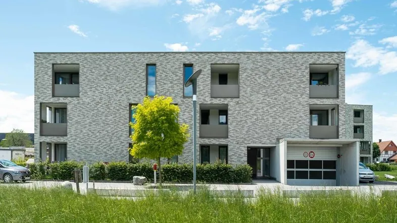 Modernes Mehrfamilienhaus mit grauer Klinkerfassade, Balkonen und integrierter Tiefgarage.