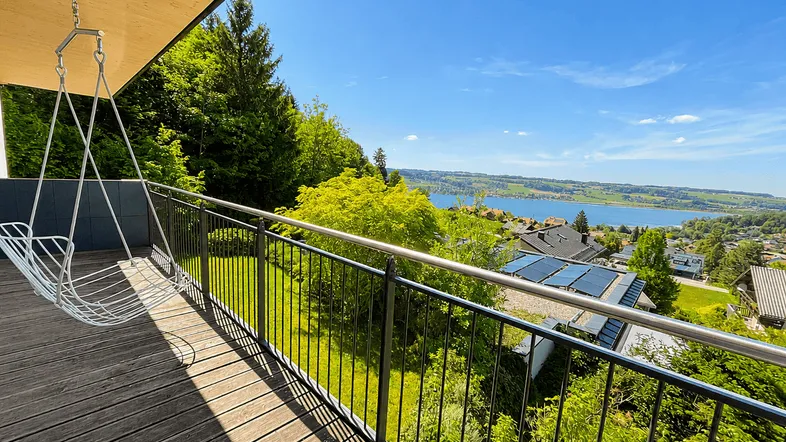 Geräumiger Balkon mit Holzboden, Schaukelstuhl und weitem Blick auf den See und die Landschaft.