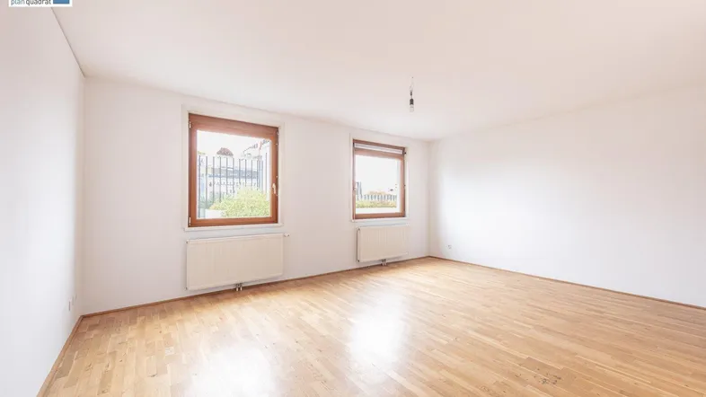 Helles, leeres Zimmer mit Parkettboden und zwei Fenstern, bereit zur individuellen Gestaltung.
