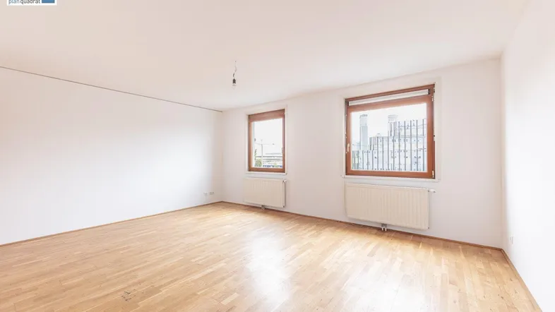 Helles, leeres Zimmer mit Parkettboden und zwei Fenstern, bereit zur individuellen Gestaltung.