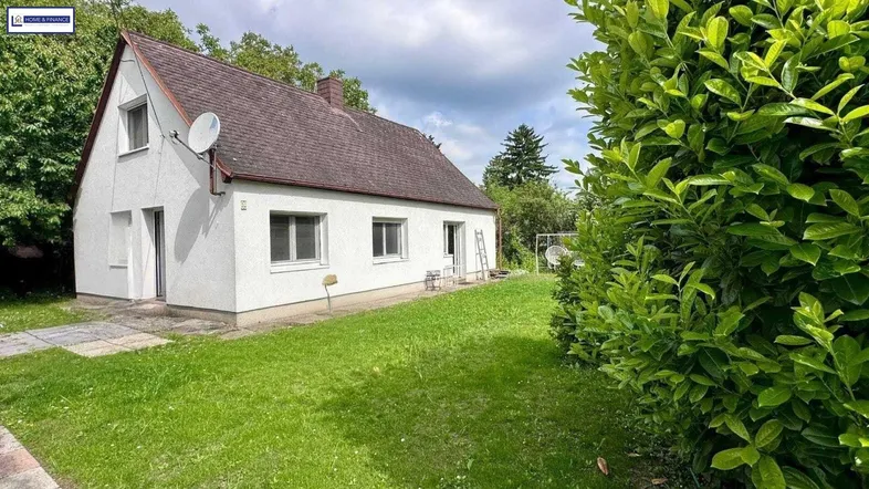 Freistehendes Einfamilienhaus mit weißer Fassade, braunem Satteldach und großem Gartenbereich.