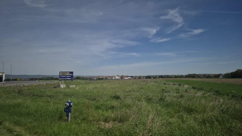 Weitläufiges unbebautes Grundstück mit grüner Wiese und einem Hinweisschild unter blauem Himmel.