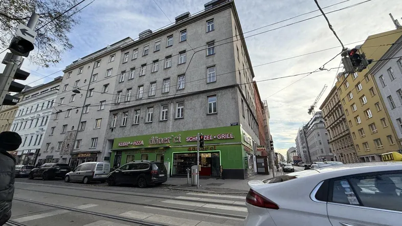 Gebäudeansicht an einer belebten Straße mit Geschäften im Erdgeschoss und darüberliegenden Wohnungen.