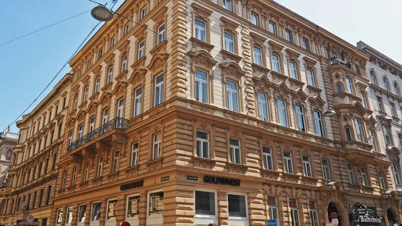 Großes, historisches Eckgebäude mit reich verzierter Fassade und Geschäften im Erdgeschoss an einer belebten Straße.