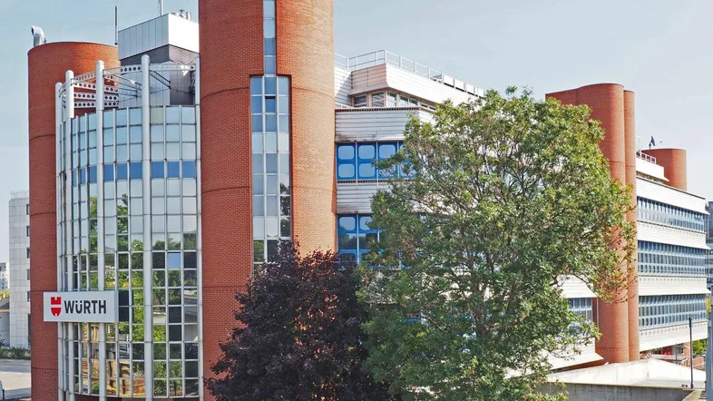 Großes Geschäftsgebäude mit markanter Ziegel- und Glasfassade, umgeben von Bäumen unter blauem Himmel.