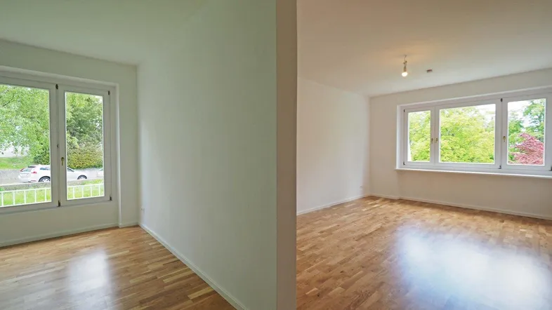 Helle, leere Räume mit Parkettboden und großen Fenstern, die viel Tageslicht hereinlassen.