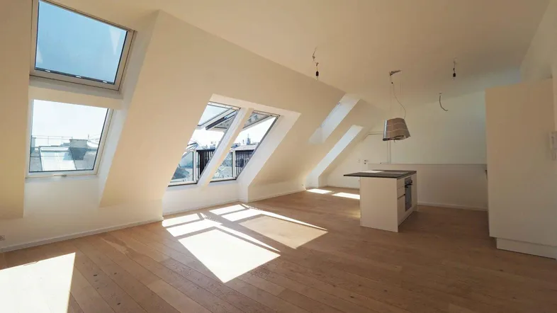 Helles Dachgeschosszimmer mit Holzboden, Dachfenstern und einem Küchenblock.