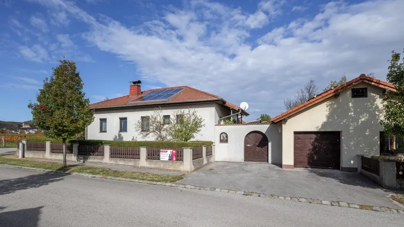 Ansicht des Hauses von der Straße mit Garage, Zaun und Photovoltaikanlage auf dem Dach.