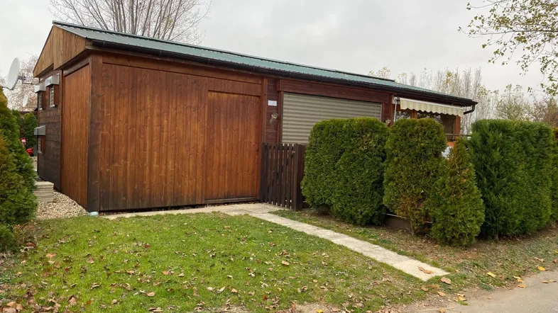 Holzverkleidetes Gebäude mit grünem Dach und kleinem Vorgarten, umgeben von Hecken.