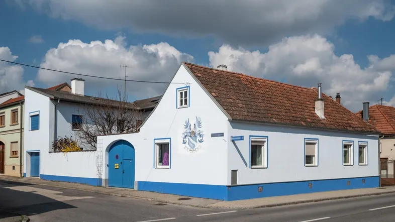 Weißes Haus mit blauen Akzenten und Wappen an der Fassade unter blauem Himmel.