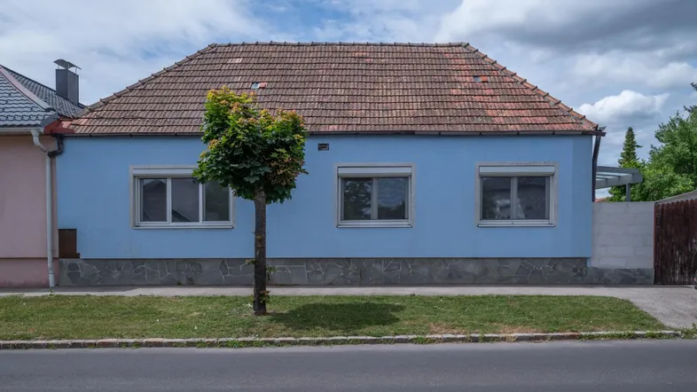 Blau gestrichenes Einfamilienhaus mit Ziegeldach und kleinen Fenstern zur Straße hin.