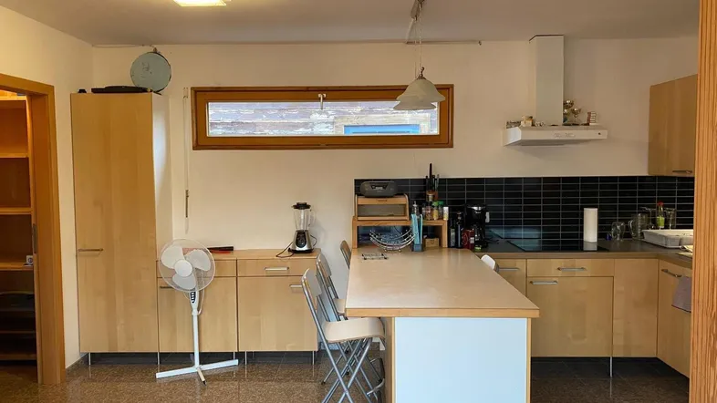 Helle Küche mit Holzschränken, schwarzem Fliesenspiegel und einer Kücheninsel mit Sitzgelegenheit.
