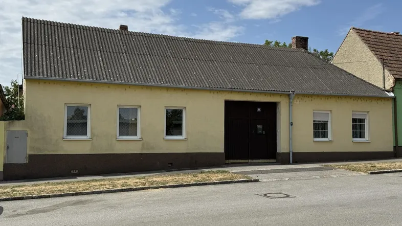 Gelbes Einfamilienhaus mit braunem Sockel, Satteldach und großer Garageneinfahrt an einer ruhigen Straße.