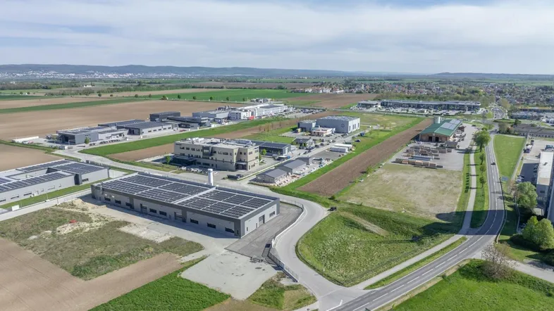 Luftaufnahme eines Gewerbegebiets mit mehreren Gebäuden, Solaranlagen und umliegenden Feldern.