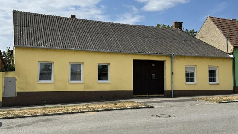 Gelbes Einfamilienhaus mit dunklem Dach und großer Garageneinfahrt an einer ruhigen Straße.