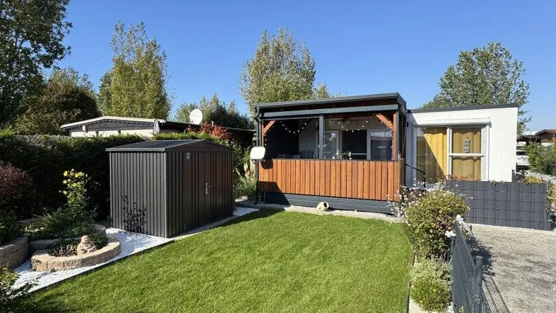 Blick auf den gepflegten Garten mit Rasenfläche, Gartenhaus und der Terrasse des Hauses.