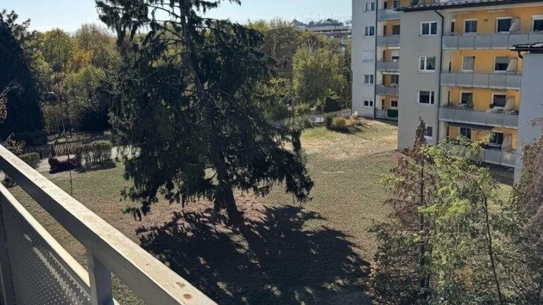 Blick vom Balkon auf eine grüne Umgebung mit Bäumen und einem angrenzenden Wohngebäude.