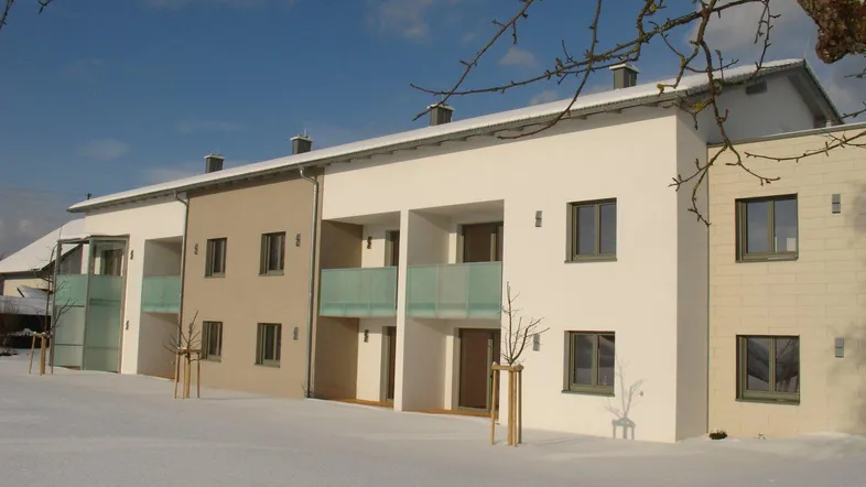 Modernes Mehrfamilienhaus mit Balkonen und schlichter Fassade, umgeben von Schnee im Winter.