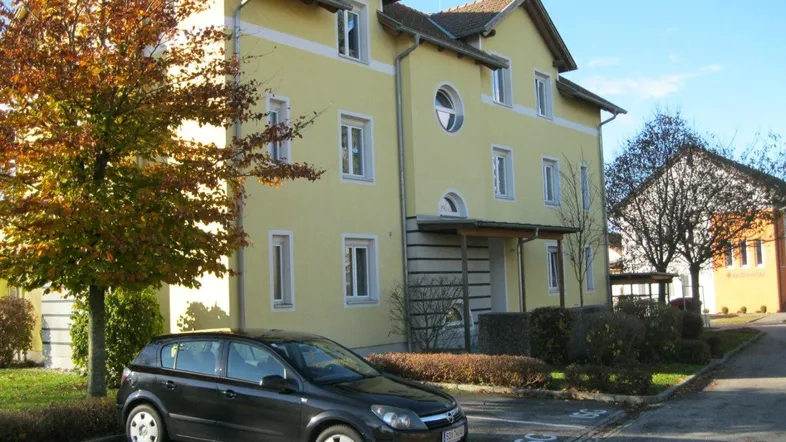 Gelbes Mehrfamilienhaus mit moderner Architektur, Parkplätzen und gepflegter Grünanlage unter blauem Himmel.