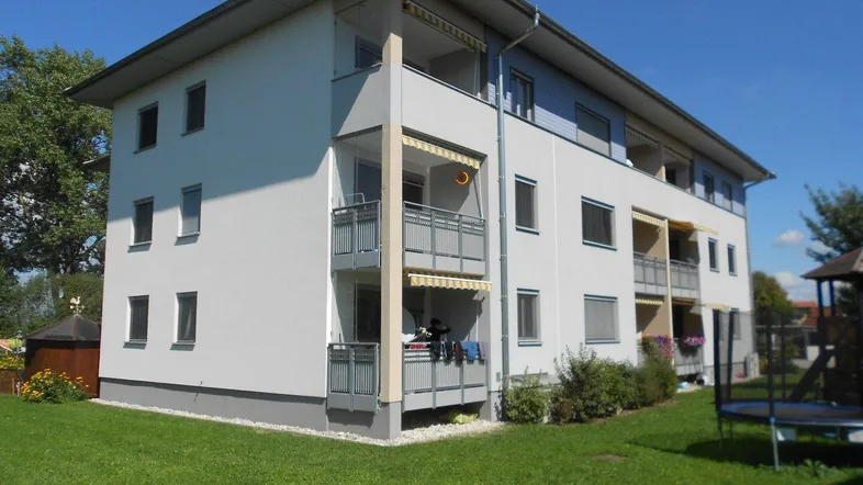 Modernes Mehrfamilienhaus mit Balkonen, gepflegter Grünfläche und Trampolin im Gartenbereich.