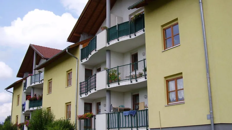 Gelbes Mehrfamilienhaus mit mehreren Balkonen und Satteldach in grüner Umgebung.