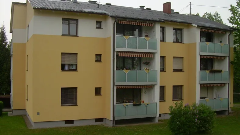 Mehrfamilienhaus mit gelb-weißer Fassade, mehreren Balkonen und einer gepflegten Grünfläche.