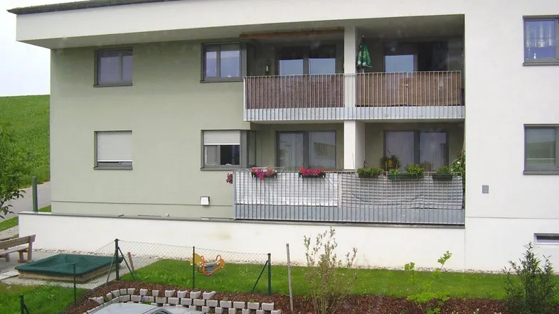 Modernes Mehrfamilienhaus mit Balkonen, Grünflächen und Parkplätzen im Freien.