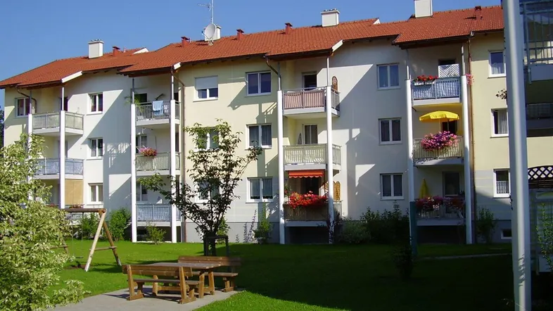 Mehrfamilienhaus mit gepflegter Fassade, Balkonen, Gemeinschaftsgarten und Spielplatz.